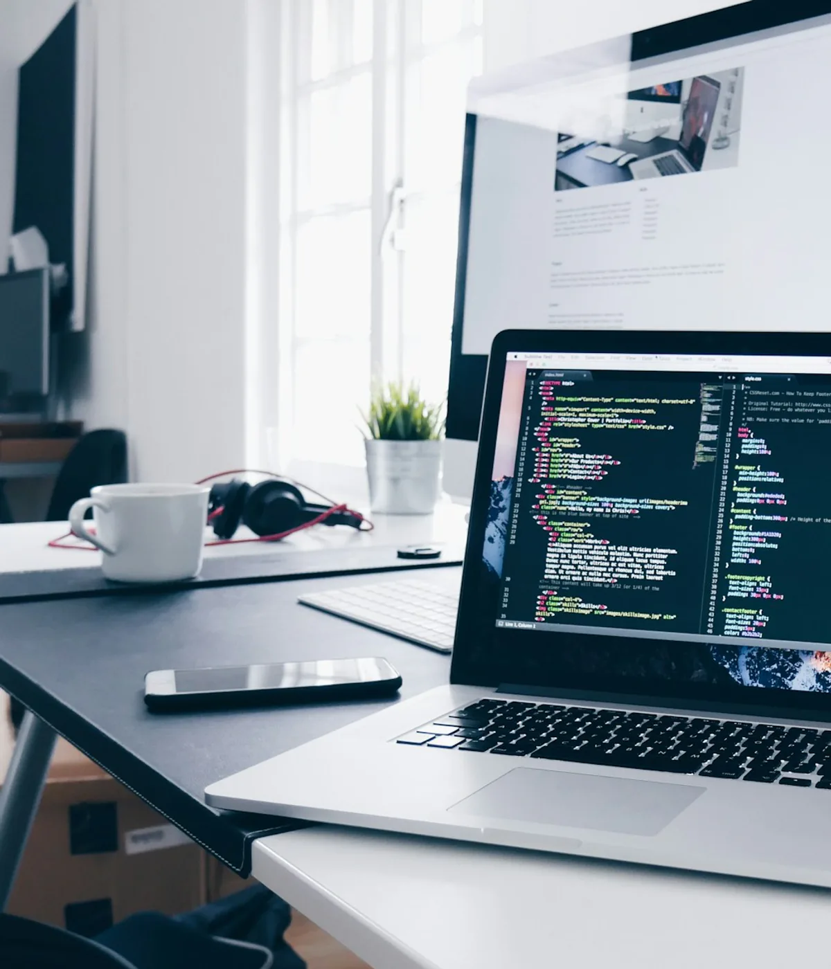 Web developer workspace with code open on a laptop and a website displayed on a desktop monitor